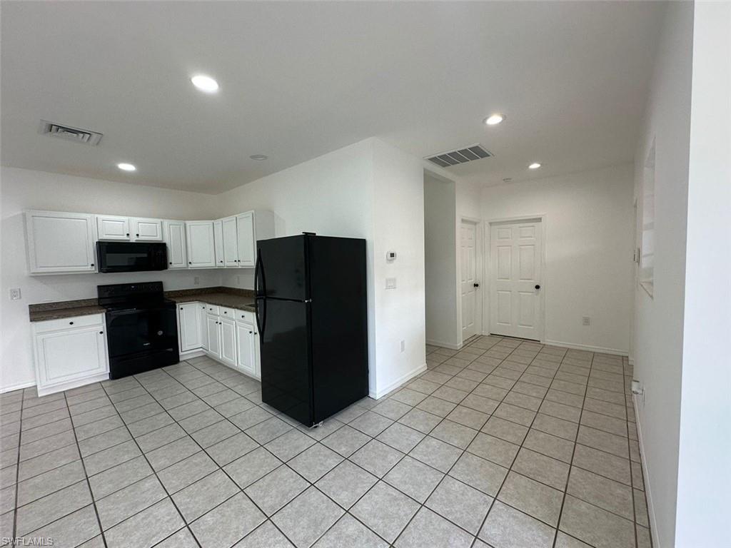Kitchen featuring white cabinetry, dark countertops, black appliances, tile flooring, and recessed lighting