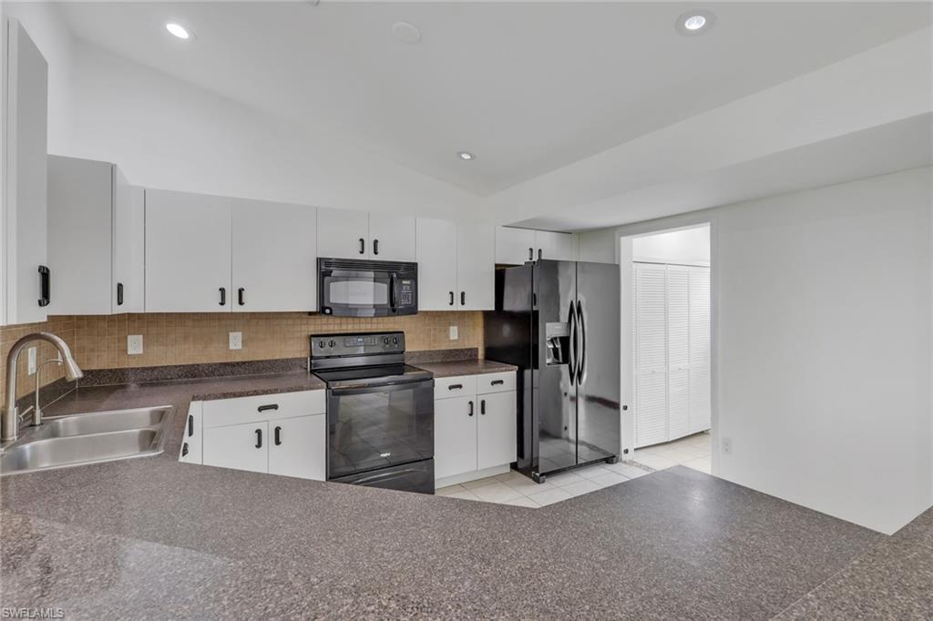 Kitchen featuring white cabinetry with black hardware, dark countertops, a stainless steel sink, a black electric range, and a black built-in microwave