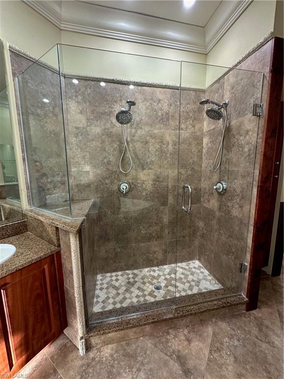 Glass-enclosed shower featuring dual shower heads, tiled walls, a mosaic tile shower pan, and a granite-clad pony wall
