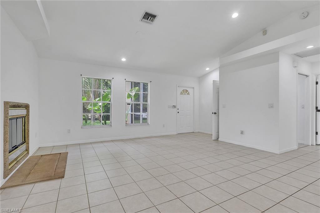 Spacious room featuring light-toned tile flooring, white walls, and a vaulted ceiling