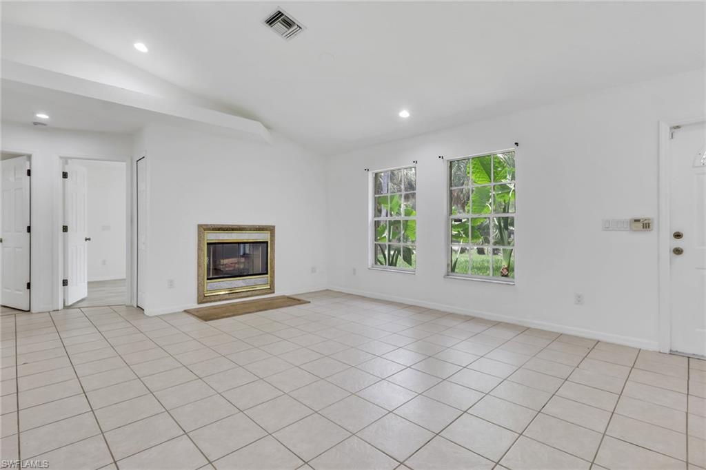 Spacious living area featuring light-toned tile flooring, an integrated fireplace with a decorative surround, and a vaulted ceiling with recessed lighting