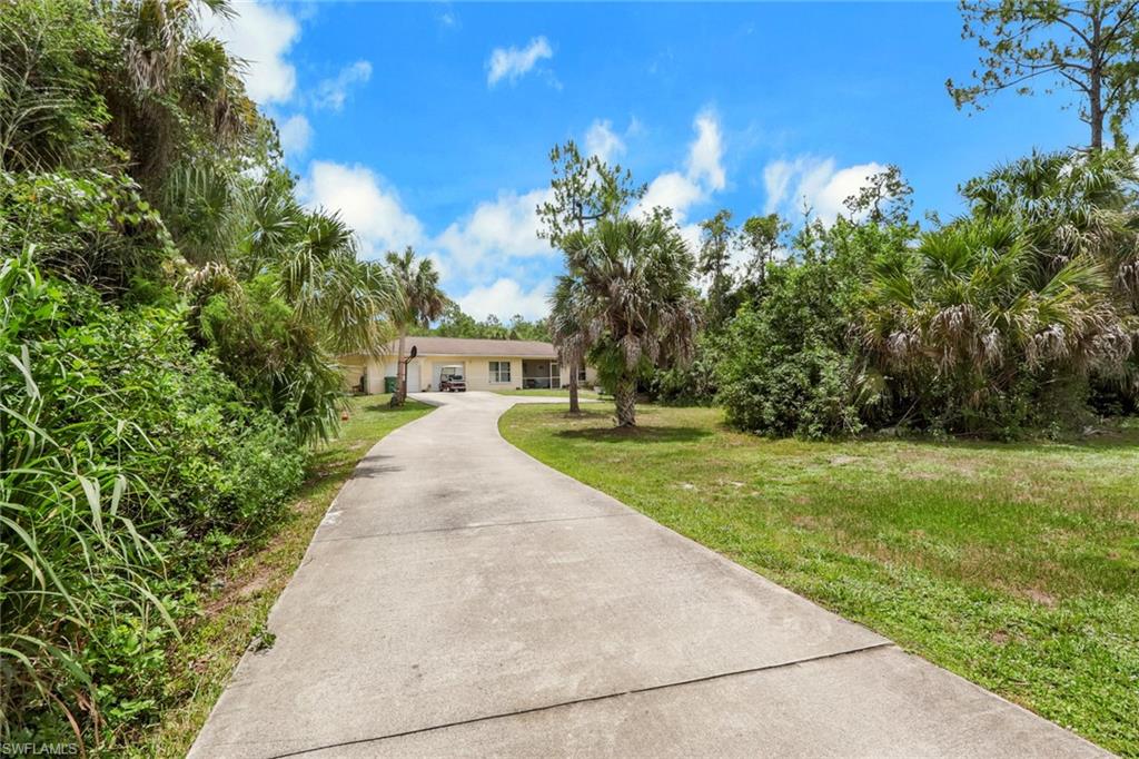 Long paved driveway leading to a single-story residence with a beige exterior
