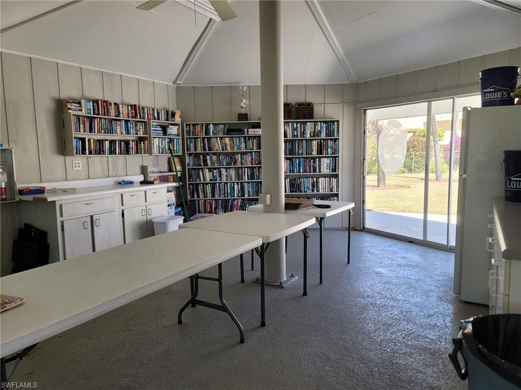Home office featuring vaulted ceiling, wooden walls, and wall of books