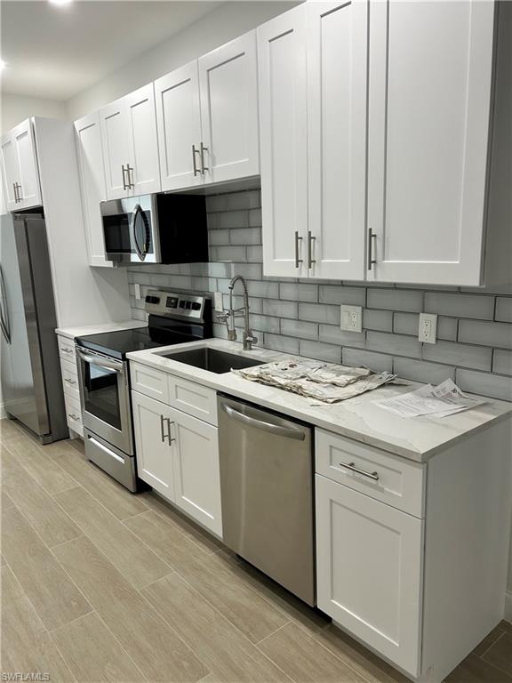 Kitchen with light hardwood / wood-style floors, decorative backsplash, light stone countertops, white cabinets, and appliances with stainless steel finishes