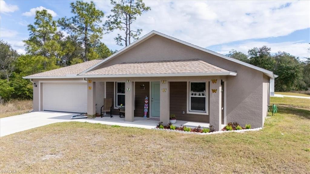 Ranch-style home with a porch, roof with shingles, stucco siding, a front lawn, and concrete driveway