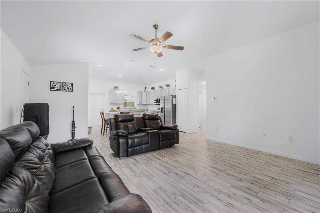 Living room with ceiling fan, light wood-type flooring, and vaulted ceiling