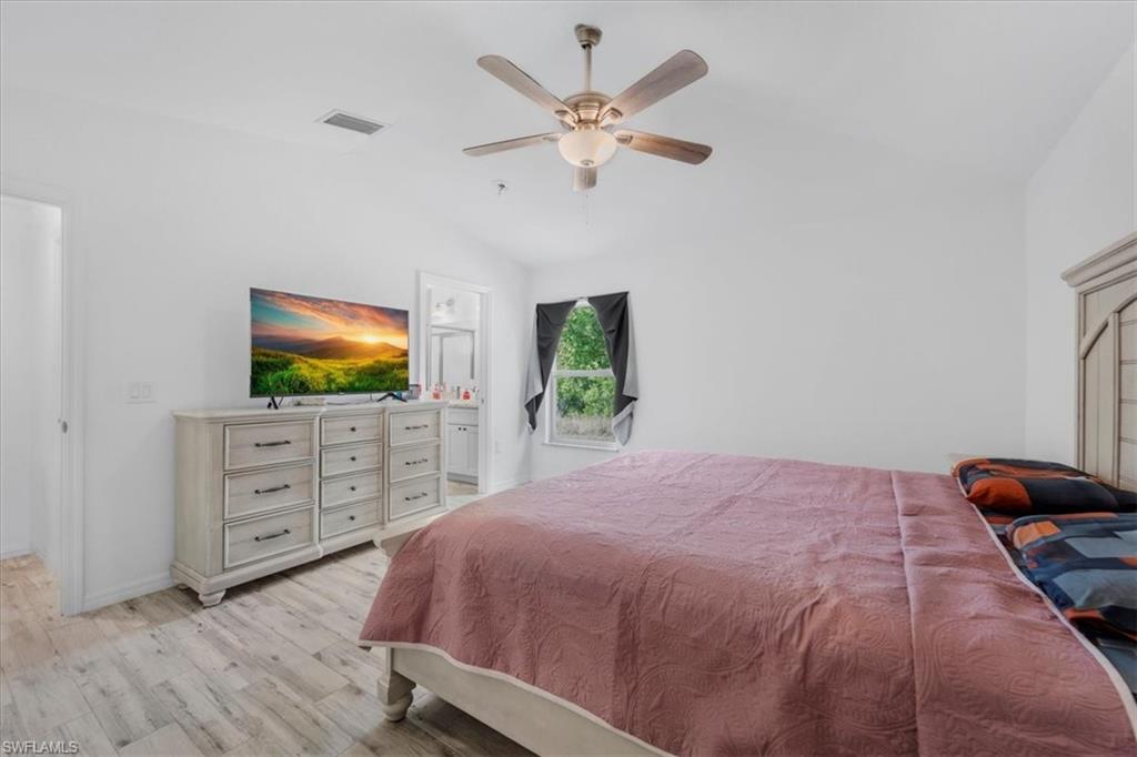 Bedroom with vaulted ceiling, light wood-style flooring, a ceiling fan, and ensuite bathroom