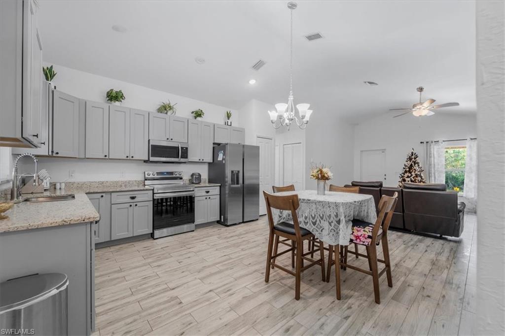 Kitchen with stainless steel appliances, hanging lights, gray cabinets, light stone countertops, and light wood-type flooring