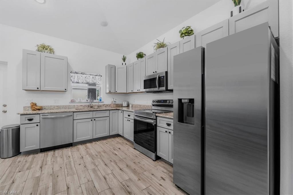 Kitchen with stainless steel appliances, light wood-style floors, gray cabinetry, and light stone counters