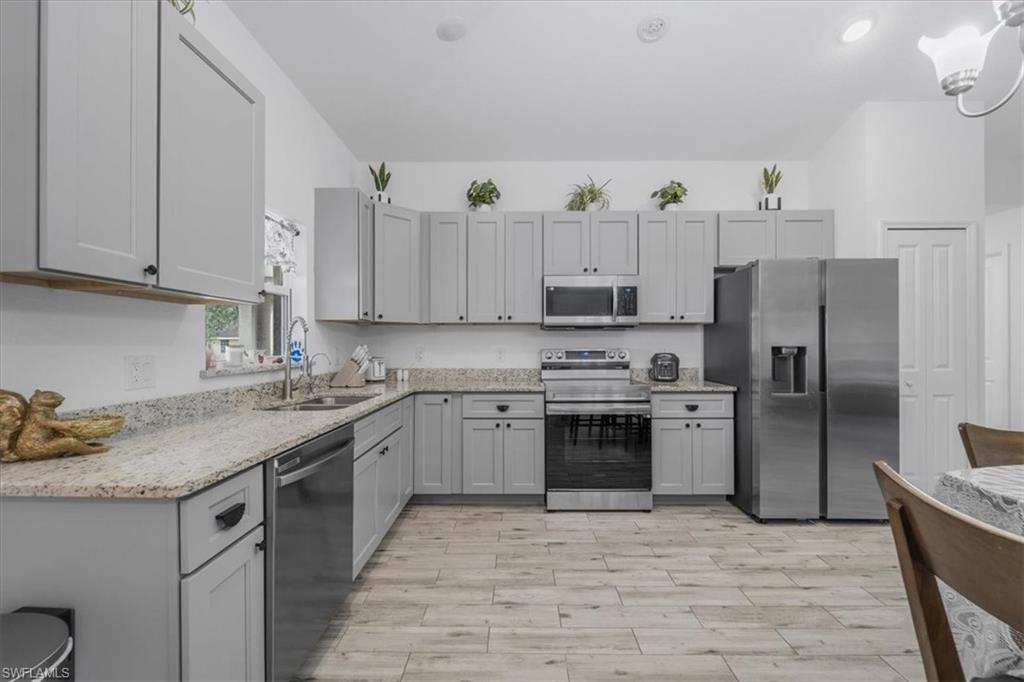 Kitchen featuring stainless steel appliances, gray cabinets, light stone counters, and wood tiled floors