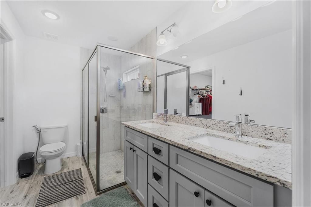 Full bathroom featuring a stall shower, a spacious closet, double vanity, and light wood-style floors