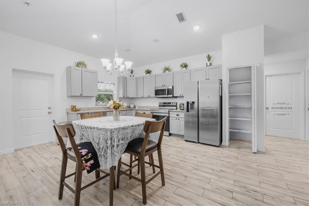Kitchen featuring gray cabinetry, stainless steel appliances, light wood-style floors, hanging lights, and light stone countertops