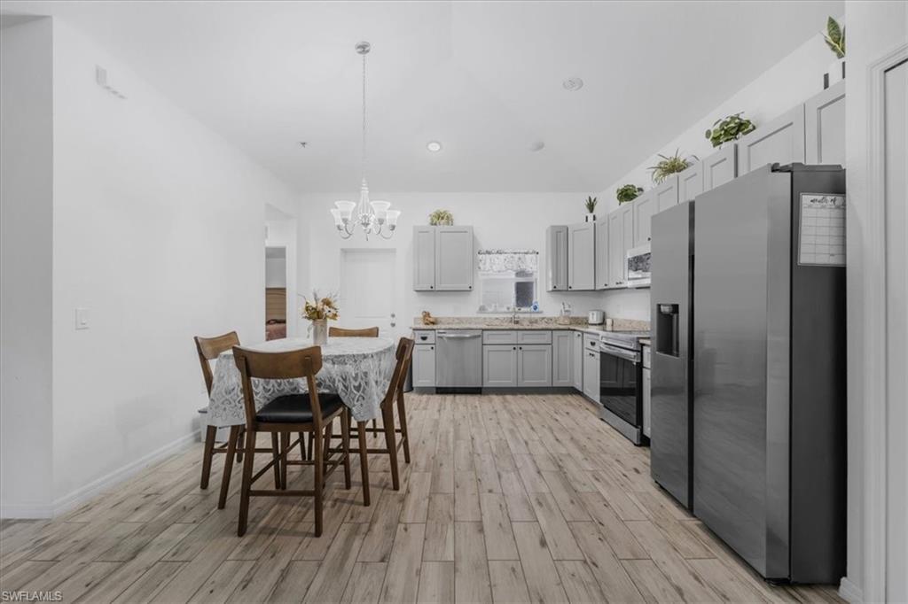 Kitchen featuring stainless steel appliances, light countertops, wood finish floors, hanging lights, and gray cabinetry