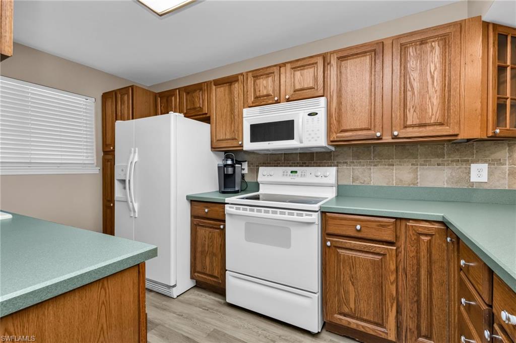 Kitchen with white appliances, wood finish cabinetry, glass fronted cabinets, light wood-type flooring, and decorative backsplash