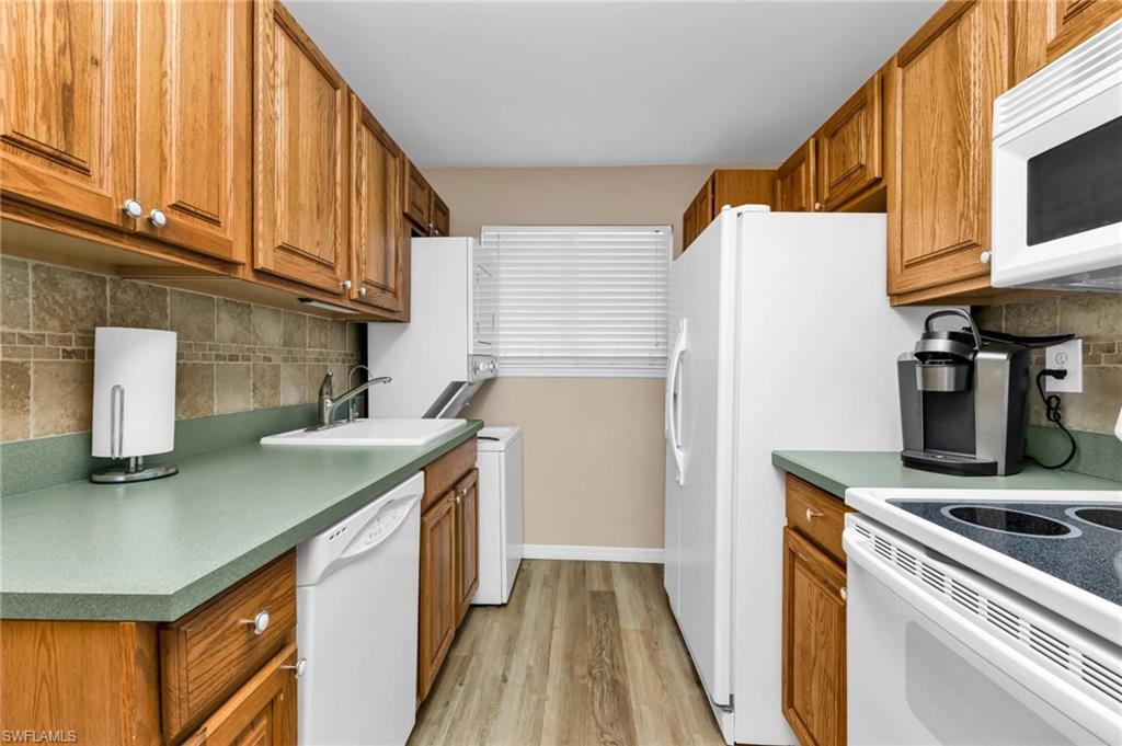Kitchen with decorative backsplash, white appliances, wood finish cabinetry, and light wood-style floors