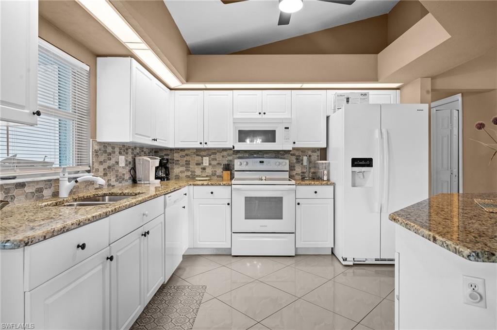 Kitchen featuring white appliances, white cabinets, dark stone countertops, a ceiling fan, and light tile patterned flooring