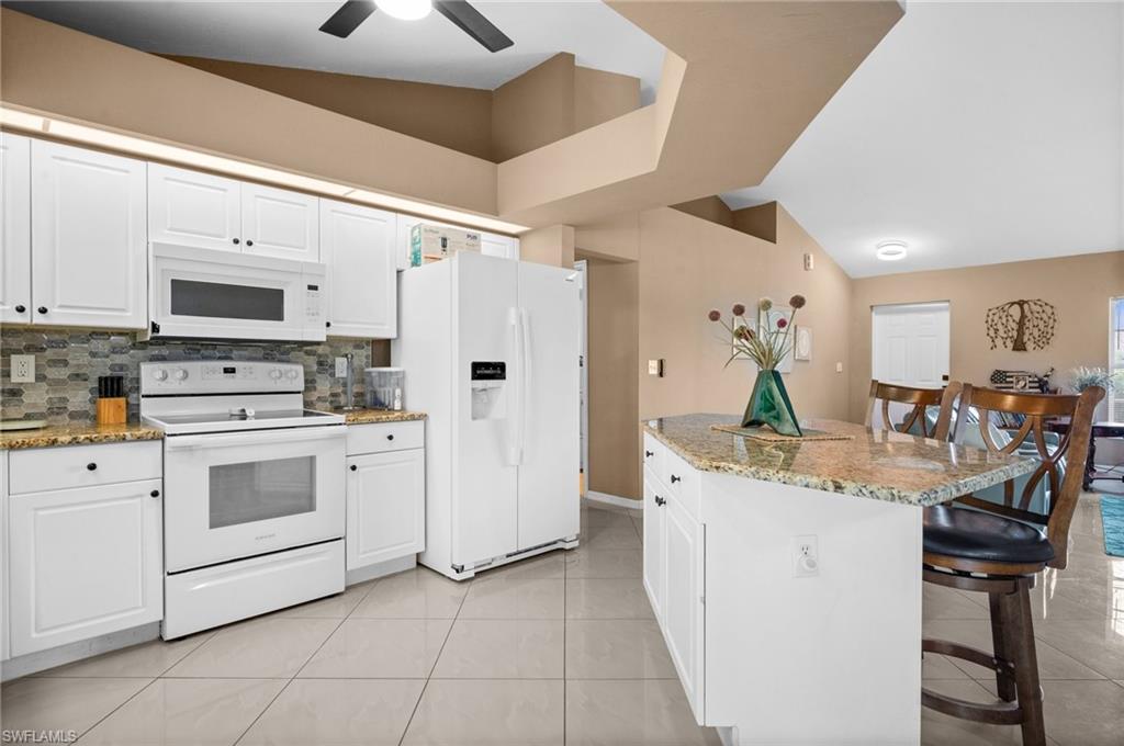 Kitchen with lofted ceiling, white appliances, white cabinets, a breakfast bar, and light stone countertops