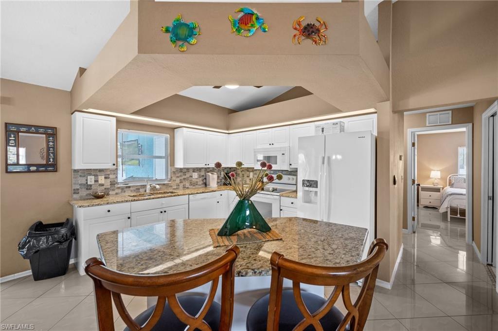Kitchen featuring light tile patterned floors, white cabinetry, a breakfast bar area, and light stone countertops