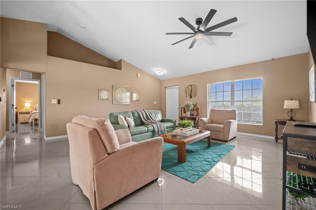 Living room with a ceiling fan, light tile patterned floors, and vaulted ceiling