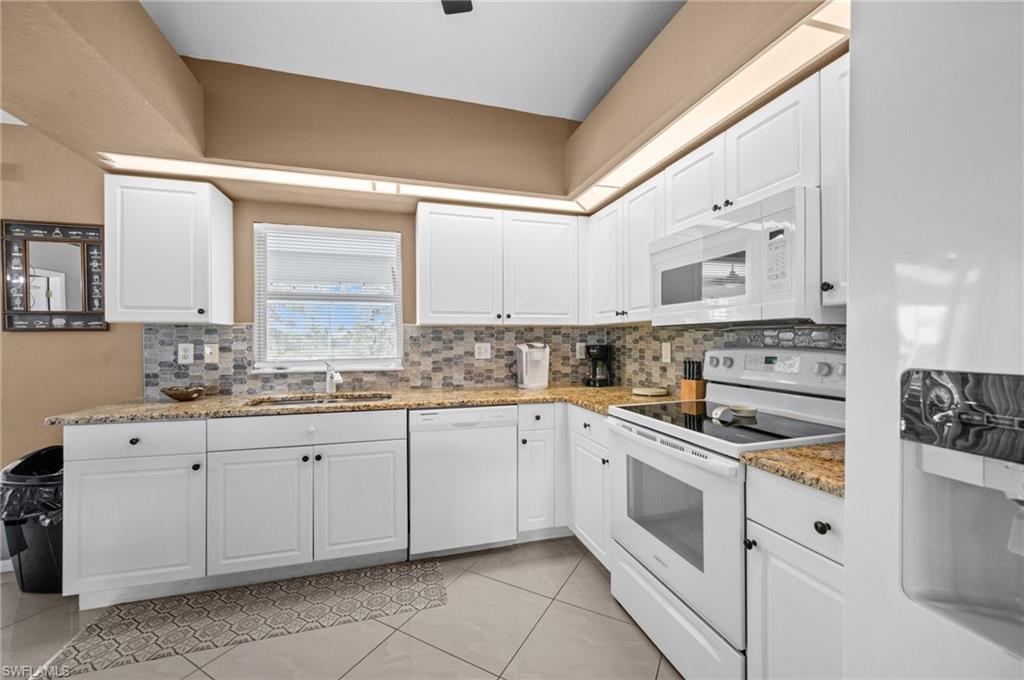 Kitchen featuring white appliances, white cabinetry, light stone countertops, and tasteful backsplash