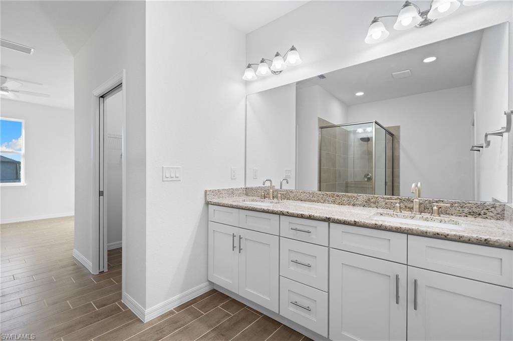 Full bathroom with a shower stall, double vanity, wood tiled floors, ceiling fan, and a spacious closet