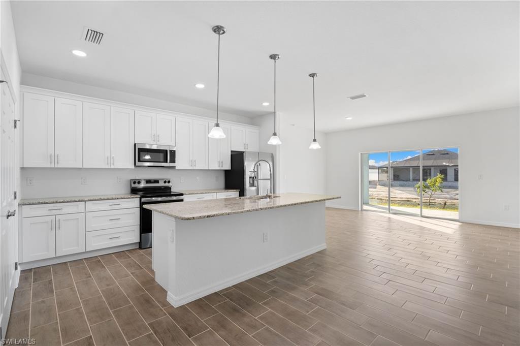 Kitchen with stainless steel appliances, light stone countertops, a kitchen island with sink, and white cabinets