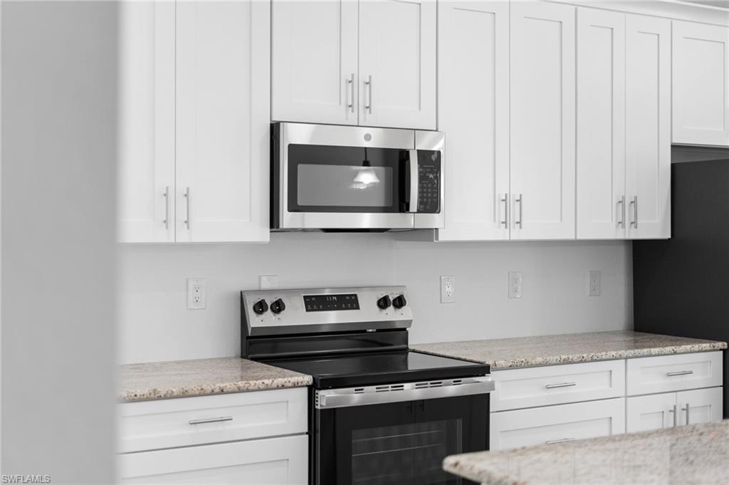 Kitchen with stainless steel appliances, white cabinetry, and light stone countertops