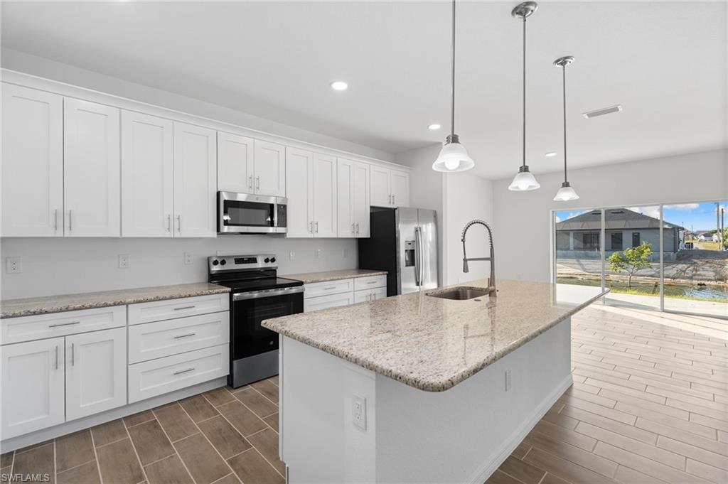 Kitchen featuring stainless steel appliances, white cabinetry, light stone counters, and wood tiled floors