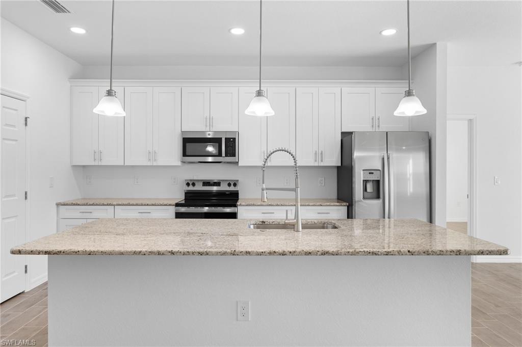 Kitchen with wood finish floors, stainless steel appliances, white cabinets, light stone counters, and hanging light fixtures