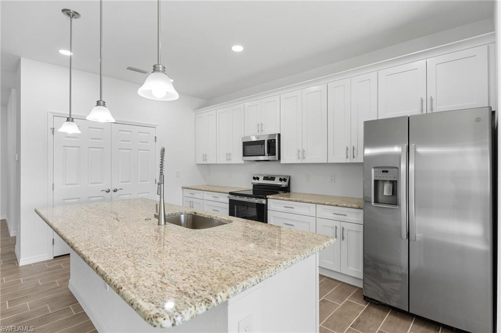 Kitchen with stainless steel appliances, wood finish floors, and white cabinetry