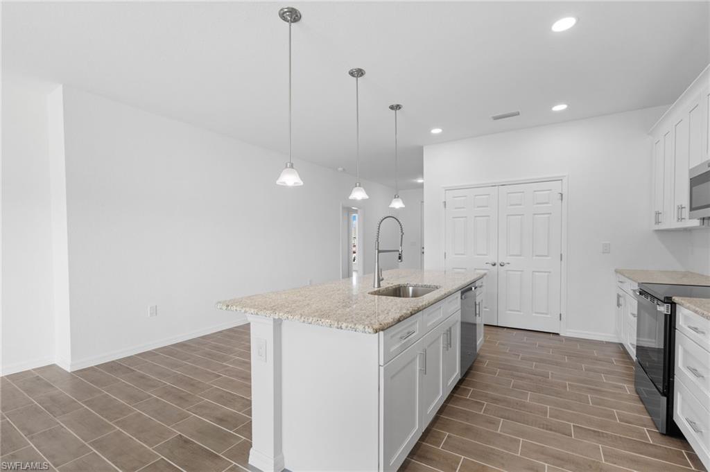 Kitchen featuring white cabinets, stainless steel appliances, decorative light fixtures, light stone counters, and an island with sink
