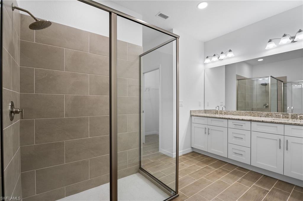 Bathroom with double vanity, a shower stall, recessed lighting, and a walk in closet