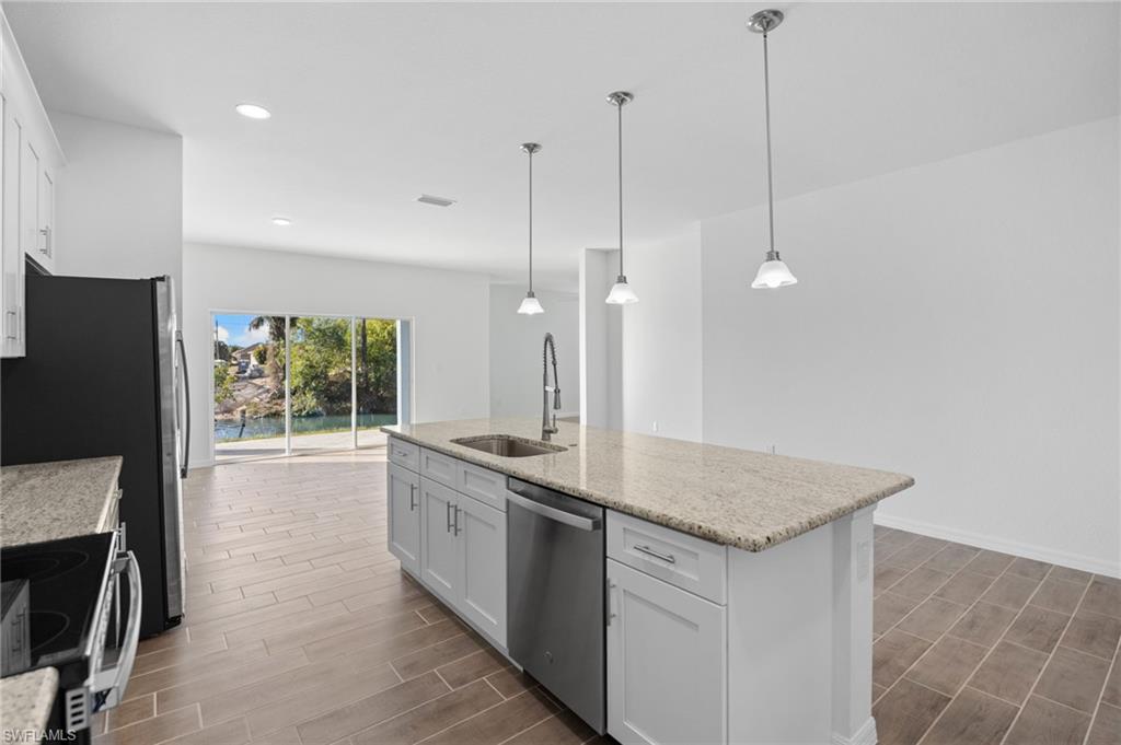 Kitchen with white cabinets, stainless steel appliances, light stone countertops, and wood tiled floors