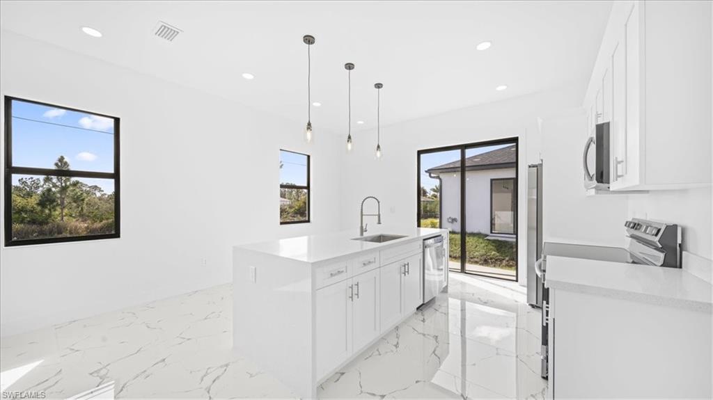 Kitchen with white cabinets, light stone counters, stainless steel appliances, and hanging light fixtures