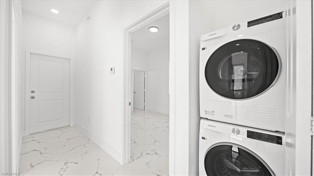 Laundry area with stacked washer / drying machine, light marble finish flooring, and recessed lighting