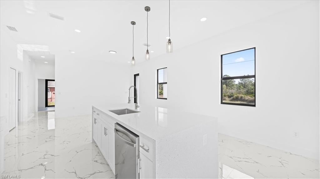Kitchen with white cabinets, pendant lighting, light stone counters, dishwasher, and a center island with sink