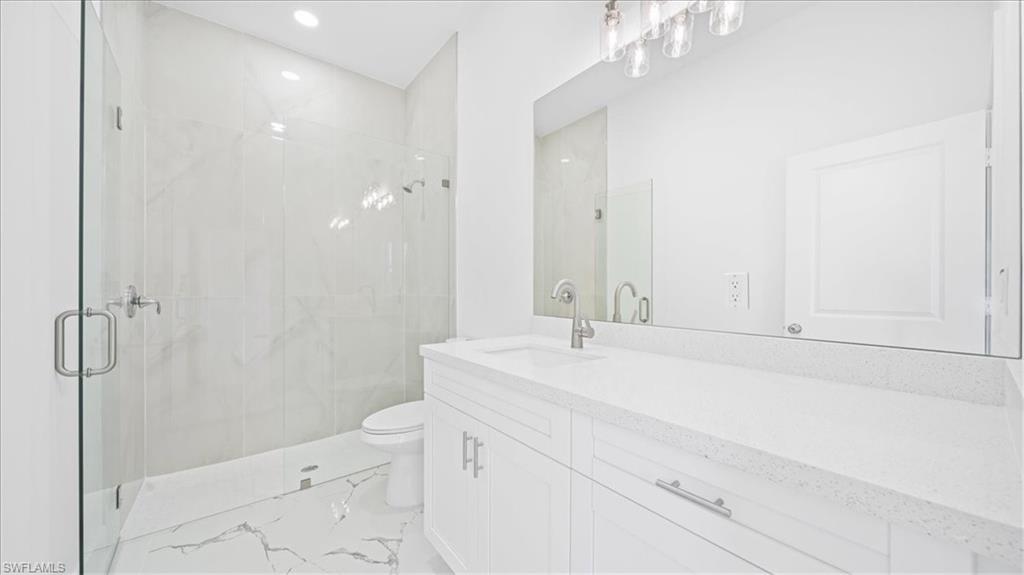 Bathroom with vanity, a marble finish shower, and recessed lighting