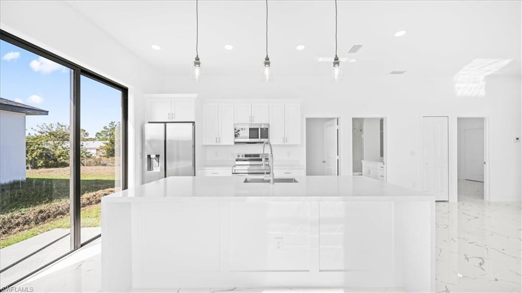 Kitchen with white cabinetry, stainless steel appliances, pendant lighting, and light stone counters