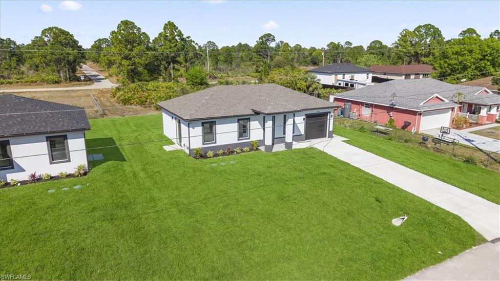 Single story home with concrete driveway, a front yard, stucco siding, and view of scattered trees