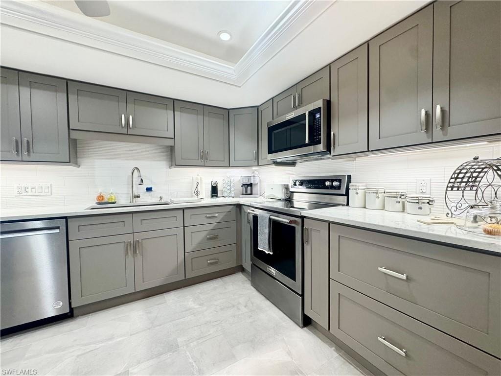Kitchen featuring gray cabinetry, stainless steel appliances, ornamental molding, light stone counters, and tasteful backsplash