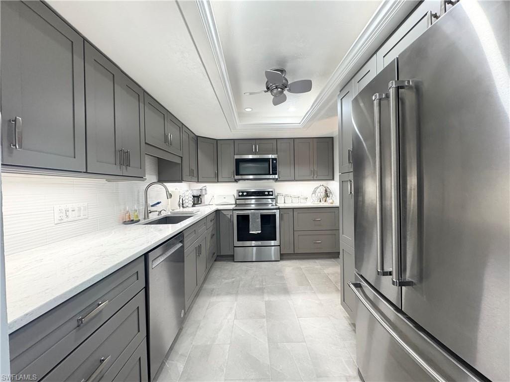 Kitchen with stainless steel appliances, gray cabinetry, a ceiling fan, light stone countertops, and a raised ceiling