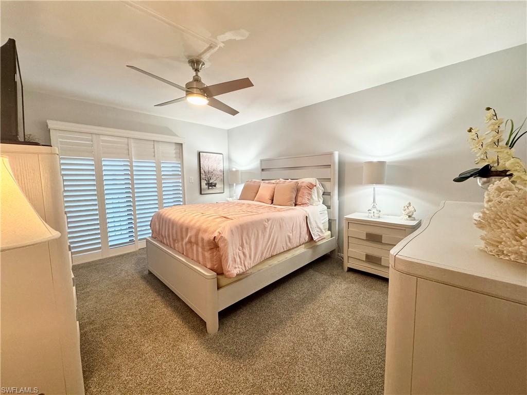 Bedroom featuring carpet and a ceiling fan.  Behind the plantation shutters is a private balcony with views of Gulf & Bay