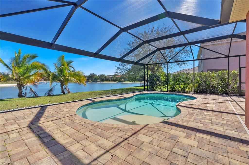 Outdoor pool with glass enclosure, a water view, a sunroom, and a patio area