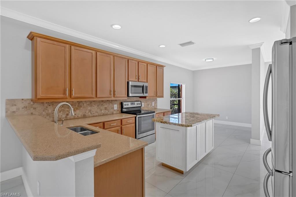 Kitchen with stainless steel appliances, light stone countertops, decorative backsplash, ornamental molding, and light marble finish flooring