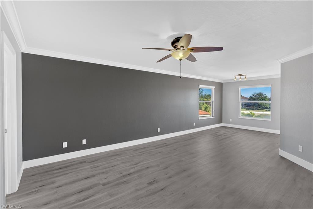 Unfurnished room with crown molding, a ceiling fan, and dark wood-style floors