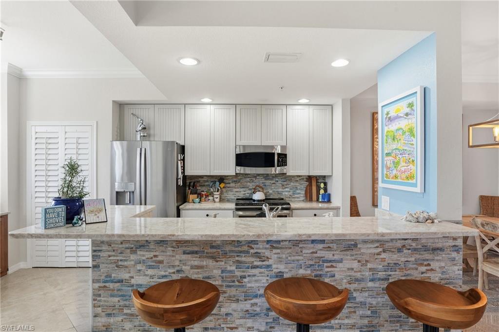 Kitchen with light stone countertops, a kitchen breakfast bar, stainless steel appliances, tasteful backsplash, and recessed lighting