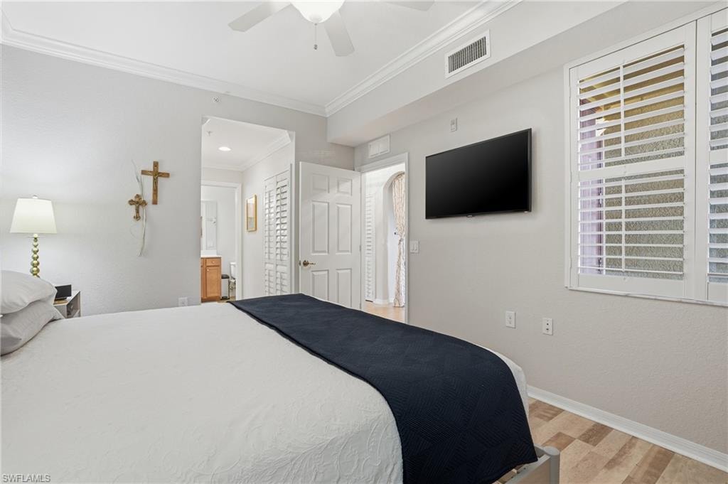 Bedroom with light wood-style floors, crown molding, a ceiling fan, and connected bathroom