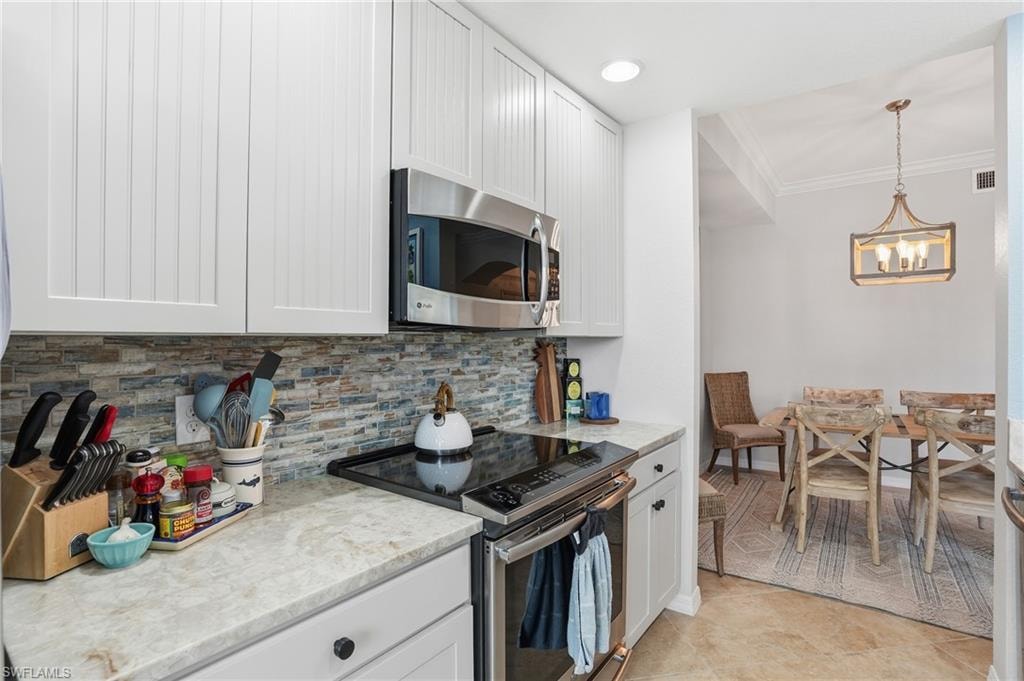 Kitchen featuring stainless steel appliances, white cabinets, pendant lighting, ornamental molding, and light stone counters