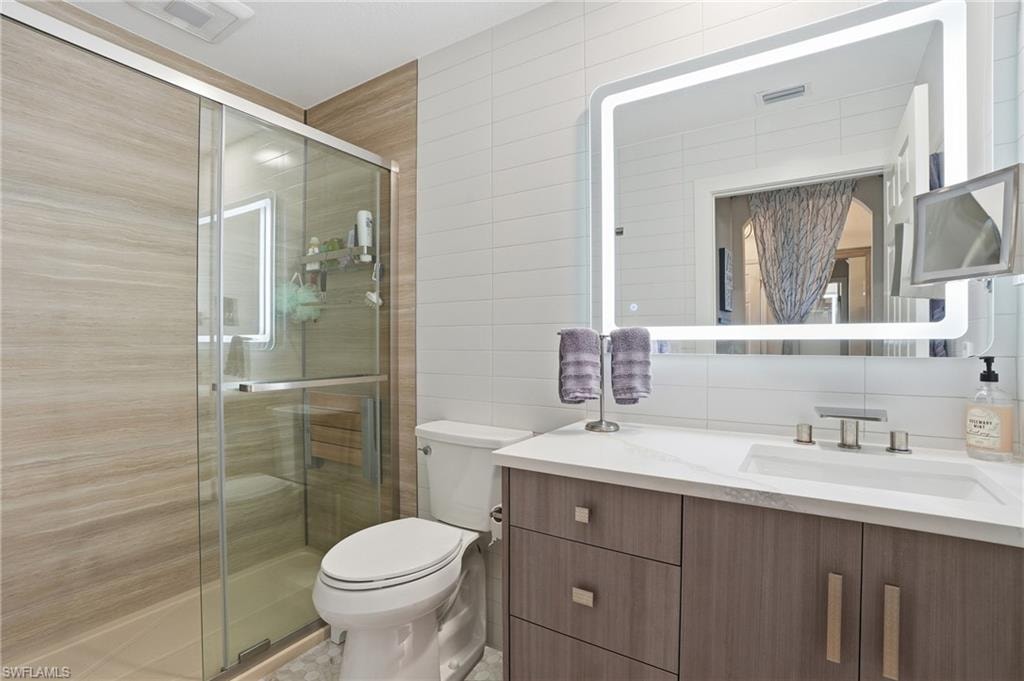 Bathroom with vanity, a shower stall, tile walls, and decorative backsplash