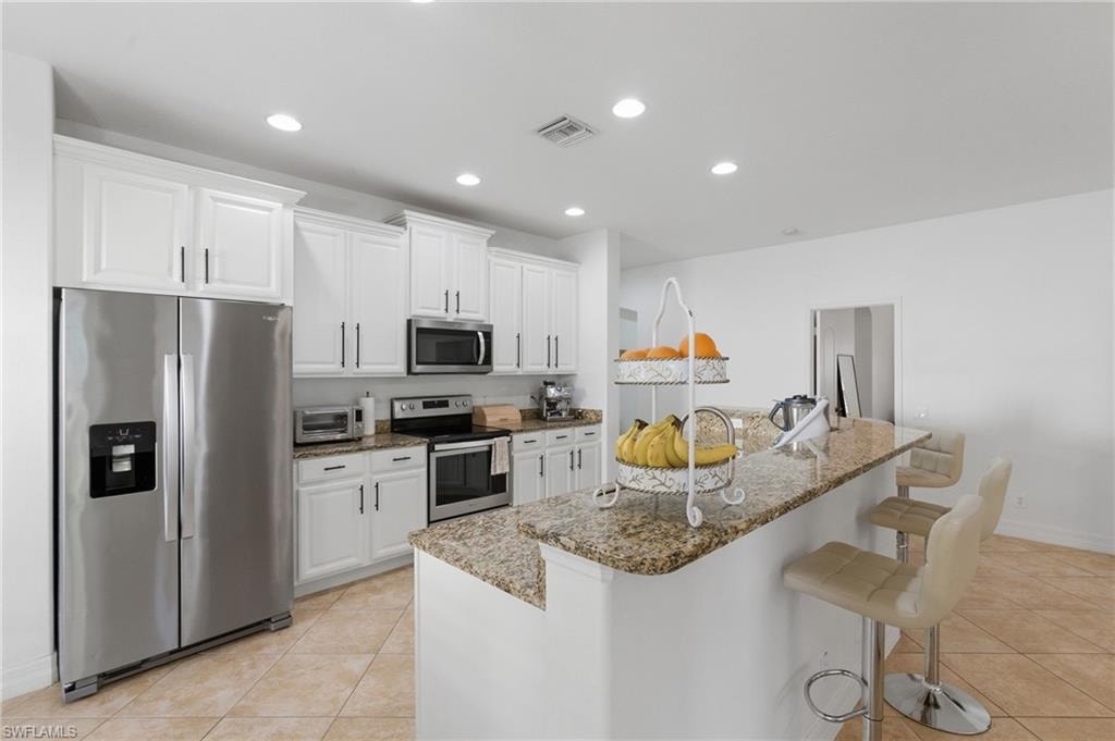 Kitchen featuring white cabinetry, stainless steel appliances, light tile patterned flooring, light stone countertops, and recessed lighting